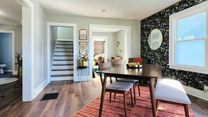 Un comedor con una mesa y sillas de madera, una alfombra roja y una escalera que lleva a otra habitación.