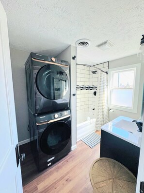 A compact laundry room with stacked appliances, a shower area, and a small sink. - Cozy 4BD - Backyard Retreat - 3mins to Notre Dame (South Bend)