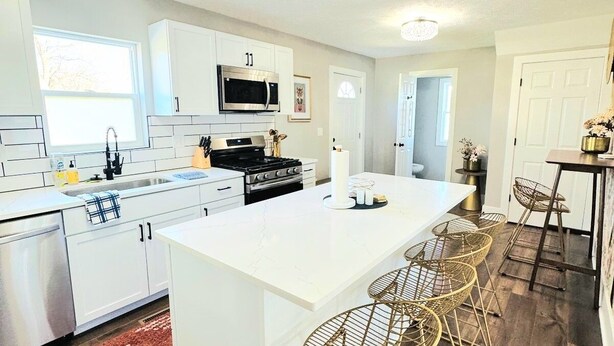 Una cocina moderna con armarios blancos, una isla grande y una zona de comedor con taburetes de bar.