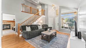 A spacious living room with a staircase, a fireplace, and a large window offering a view of the outside. - Cozy 3BR Family Home With Patio BBQ Grill Close to Casinos and Shops (Reno)