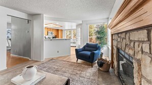 A spacious living room with a fireplace, a blue armchair, and a kitchen in the background. - Cozy 3BR Family Home With Patio BBQ Grill Close to Casinos and Shops (Reno)