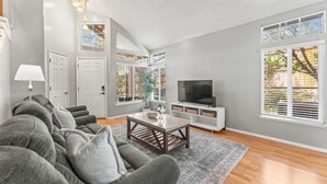 A modern living room with a grey sofa set, a wooden coffee table, a TV, and a large window with blinds. - Cozy 3BR Family Home With Patio BBQ Grill Close to Casinos and Shops (Reno)