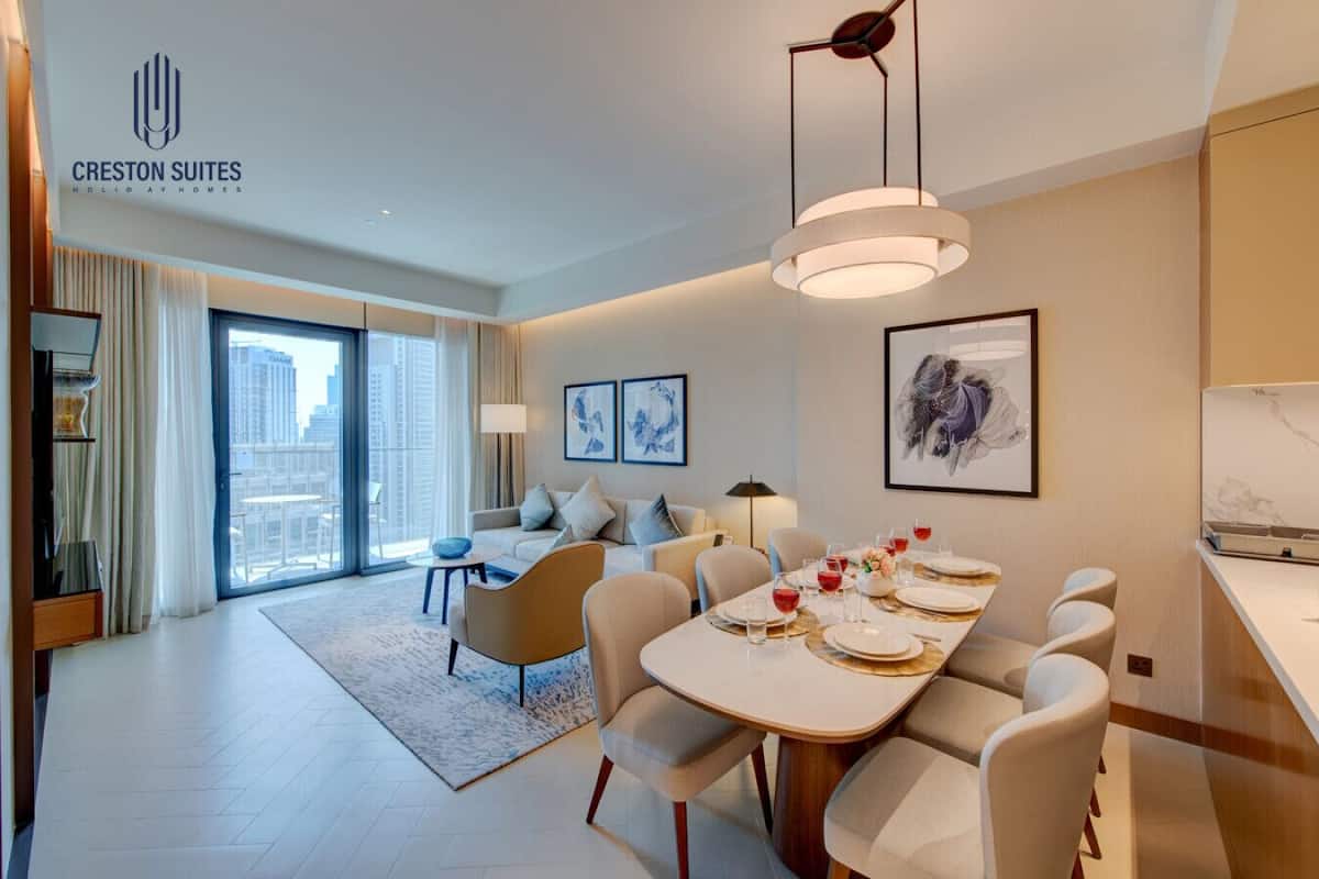 A modern hotel suite with a dining area, a sofa set, and a large window offering a city view.