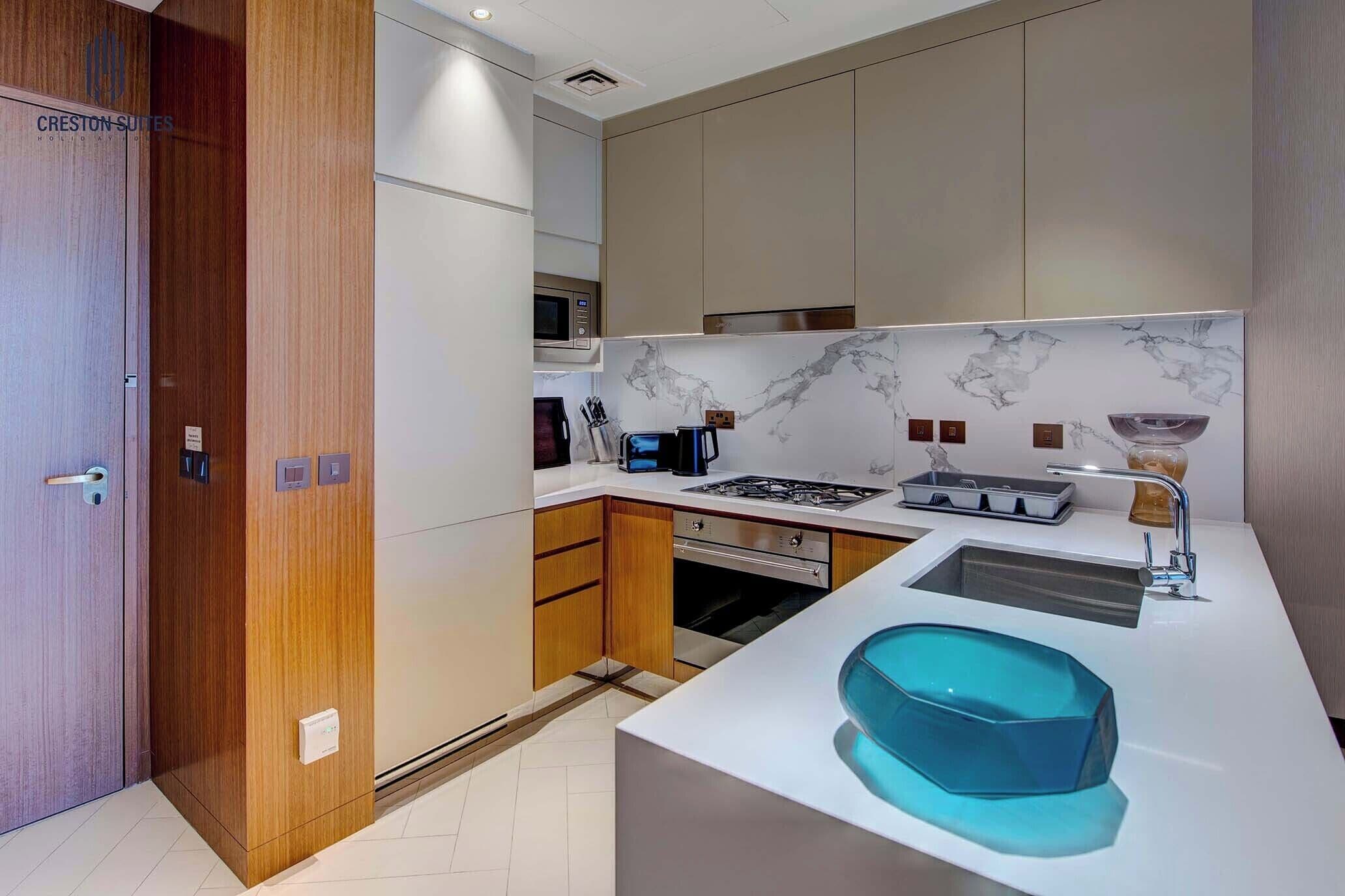 Een moderne keuken met houten kastjes, een ingebouwde magnetron, een gasfornuis en een wastafel met een blauwe kom.