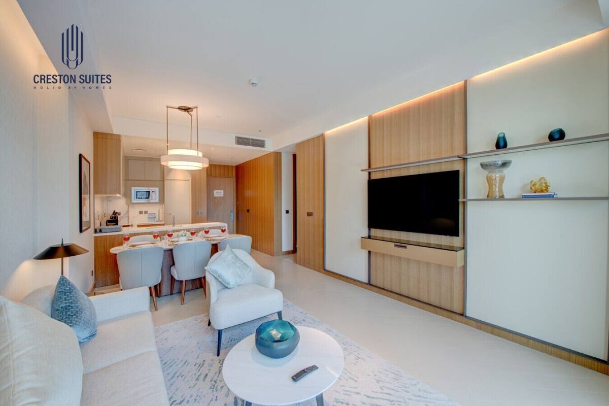A modern living room with a sofa, a coffee table, and a TV. There is a kitchen area with a dining table and chairs.