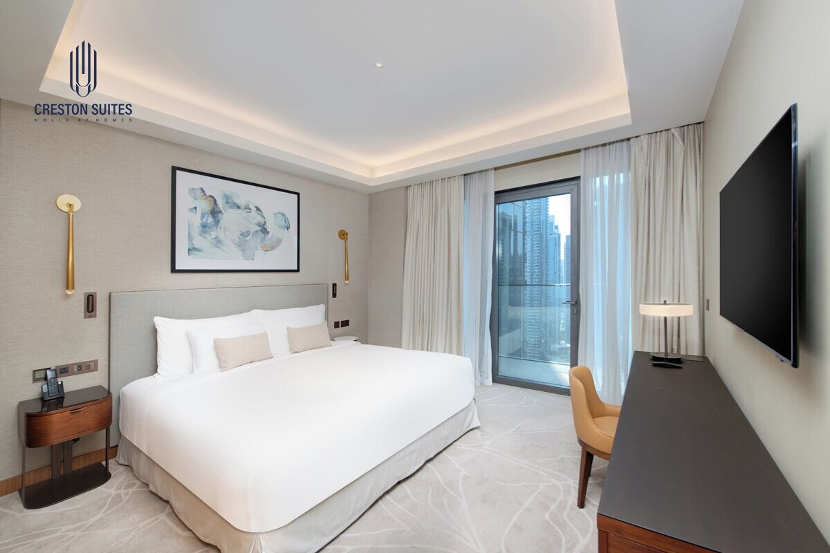 A hotel room with a large bed, a desk, a TV, and a view of the city.