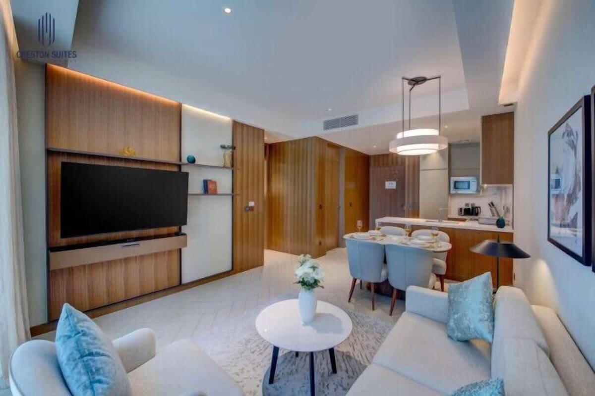 A modern living room with a flat-screen TV, a sofa set, a dining area with a small table, and a kitchen area with a microwave.