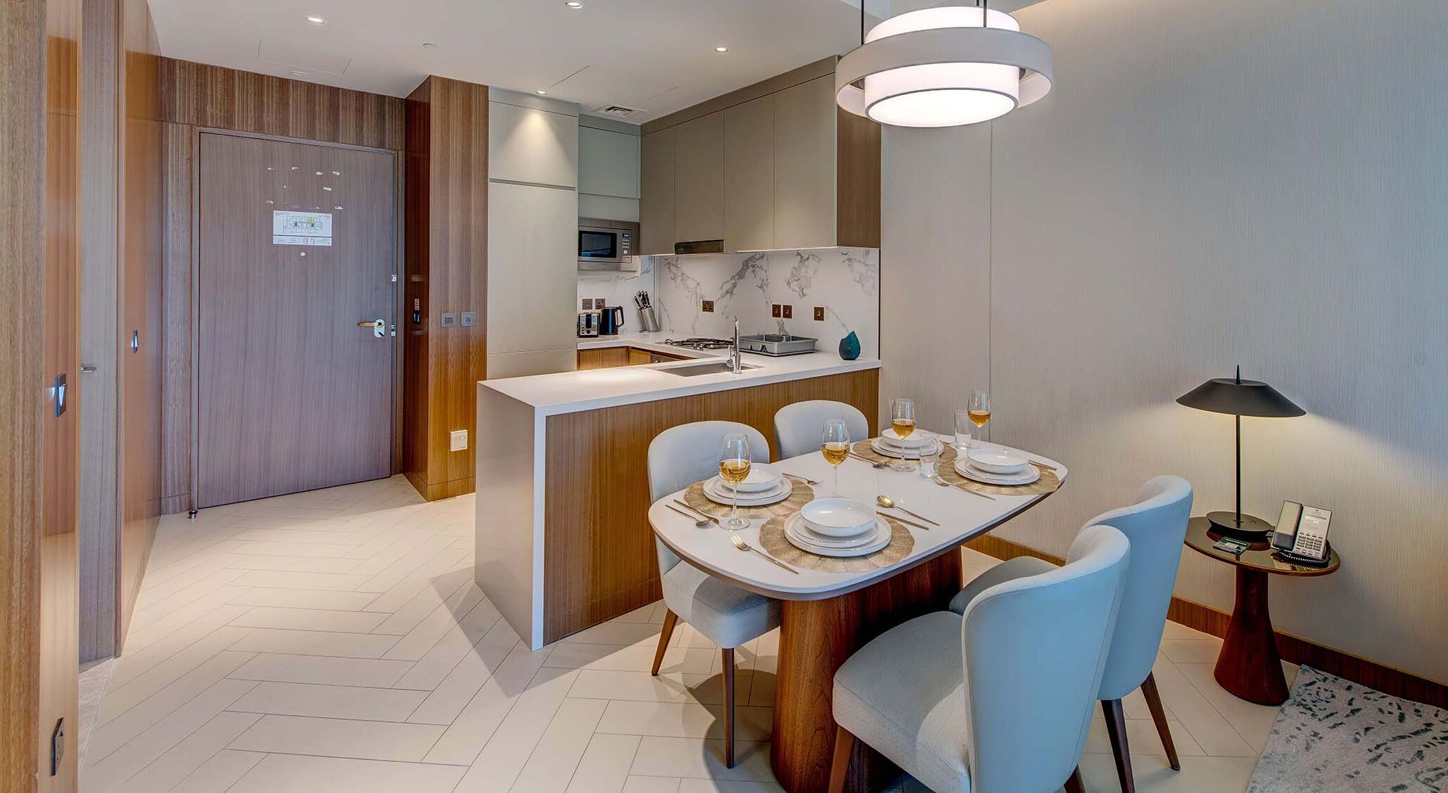 A modern dining area with a marble-top table set for four, a kitchen in the background, and a wooden door.