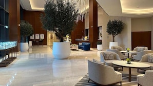 A modern lobby with a large central tree, seating areas, and a glass display case. - Creston Suites Vacation Homes Rental - Address Opera Residences (Dubai)