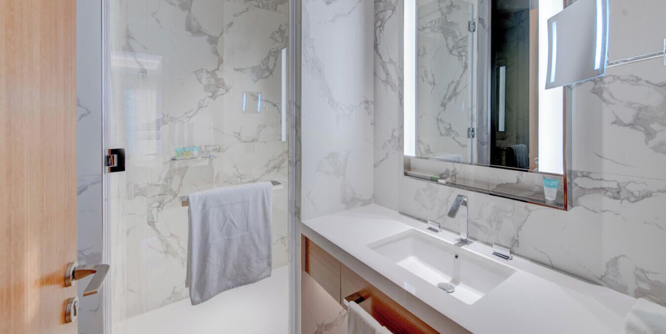 Een moderne badkamer met een marmeren spatwand, een grote spiegel en een witte wastafel.