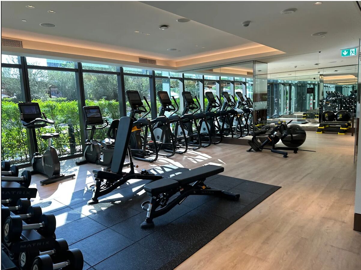 A modern gym with various exercise equipment, large windows, and a clean, well-lit interior.