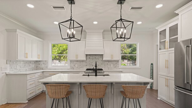 A modern kitchen with white cabinetry, a large island with bar stools, and a stainless steel refrigerator.