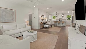 A modern living room with a white sofa, a round coffee table, and a dining area with bar stools.