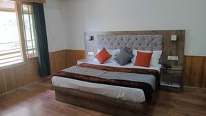 A hotel room with a large bed, wooden flooring, a headboard with a tufted design, and a window with curtains. - Tirthan Villa Resort (Banjar)