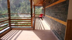 A balcony with a wooden floor and a brick wall, overlooking a mountainous landscape. - Tirthan Villa Resort (Banjar)