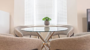 A round glass table with a central plant, surrounded by four grey upholstered chairs. - Bedford Meadows (Bedford)