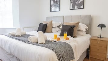 Una cama bien hecha con toallas, un plaid a rayas y dos vasos de jugo de naranja sobre una bandeja.