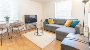 A modern living room with a grey sofa, a glass coffee table, a TV, and a small side table. - Bedford Meadows (Bedford)