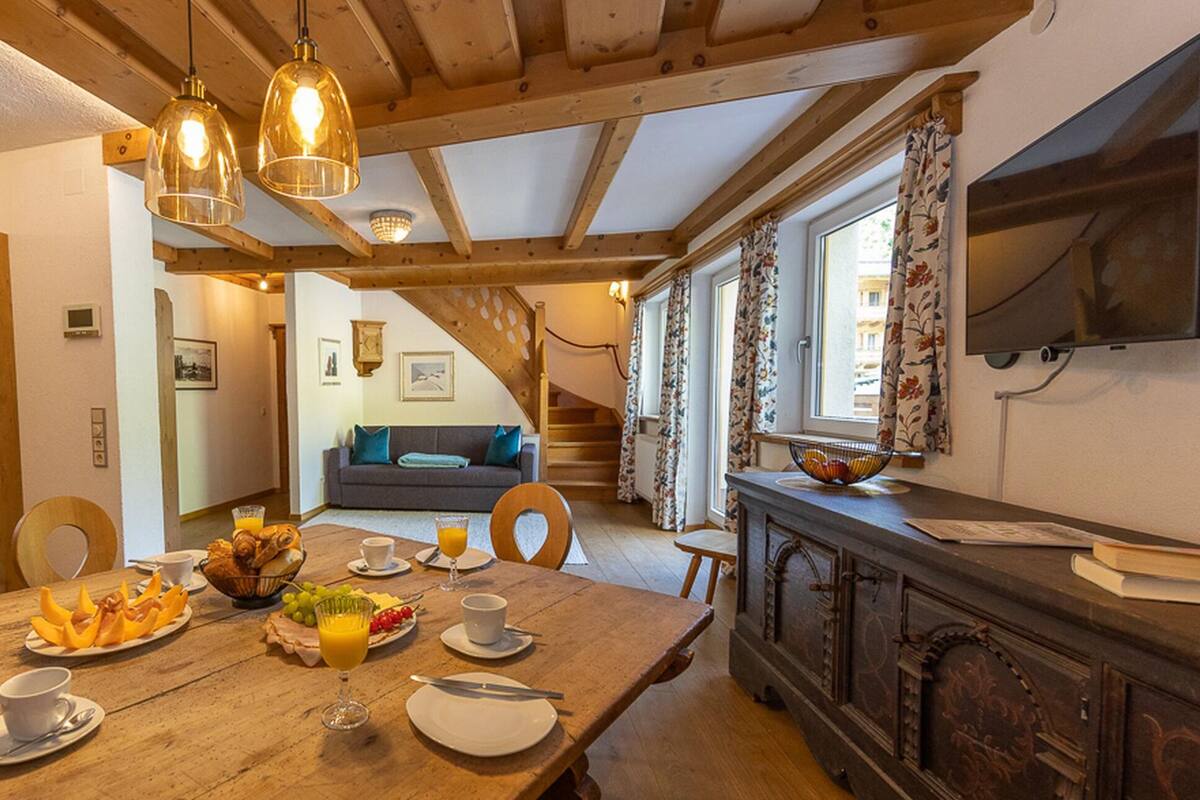 Ein Holztisch mit Frühstücksgegenständen, ein Sofa und eine Treppe, die in einen anderen Raum führt.