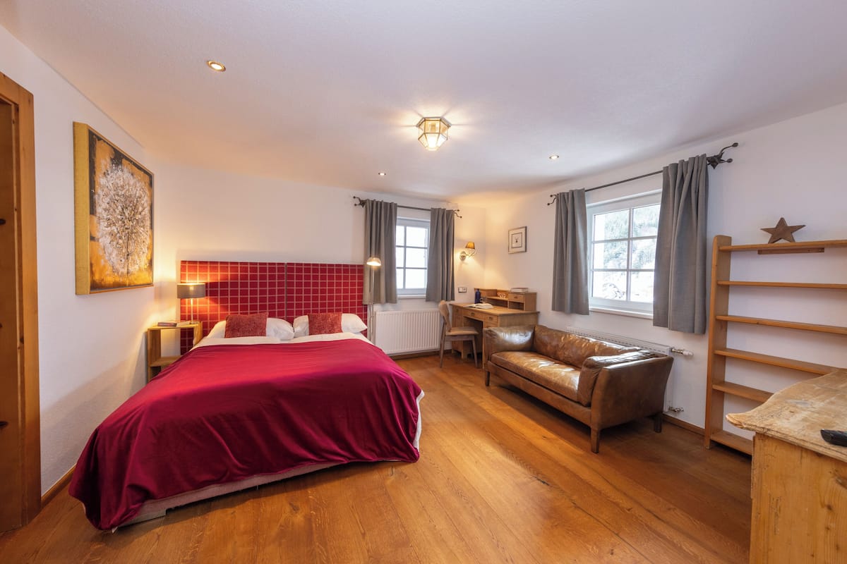 Ein Schlafzimmer mit einem großen Bett, einem Schreibtisch, einem Ledersofa und einem Fenster mit Vorhängen.