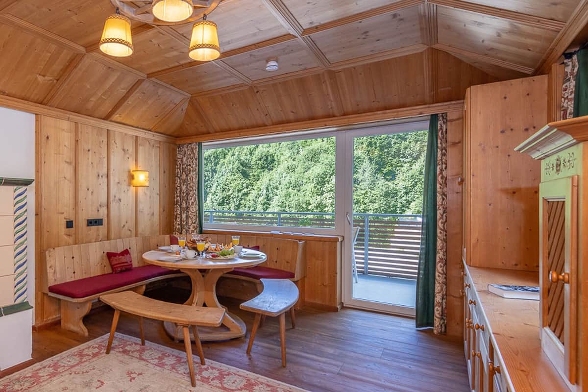 Ein gemütliches Blockhaus-Interieur mit einem Holzesstisch, Bänken und einem großen Fenster mit Blick auf grüne Natur.