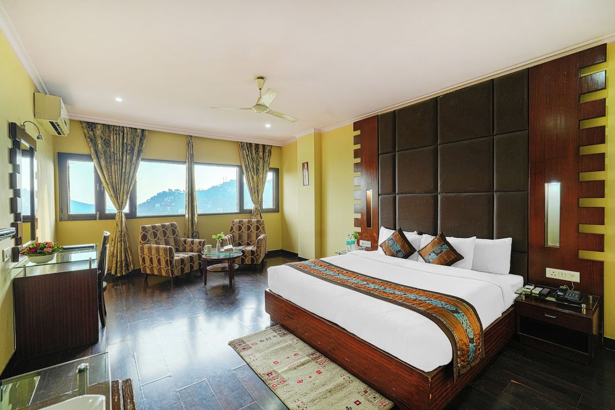 Habitación de hotel con una cama grande, un escritorio con silla, una mesita y vistas a la montaña.