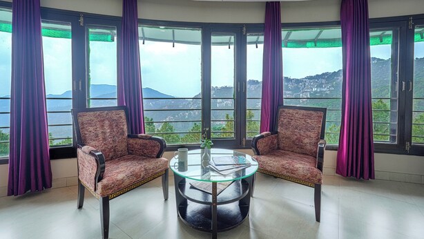 A room with two patterned chairs, a glass table, and large windows with purple curtains. - Hotel CK International By Pax Hotels (Shimla)