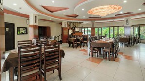 A spacious dining area with multiple tables and chairs, a central staircase, and large windows offering a view of the outdoors. - Hotel CK International By Pax Hotels (Shimla)