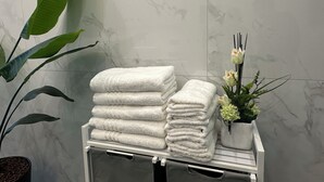 Un mucchio di asciugamani bianchi su un porta-asciugamani, con una pianta in vaso e un bouquet di fiori sullo sfondo.