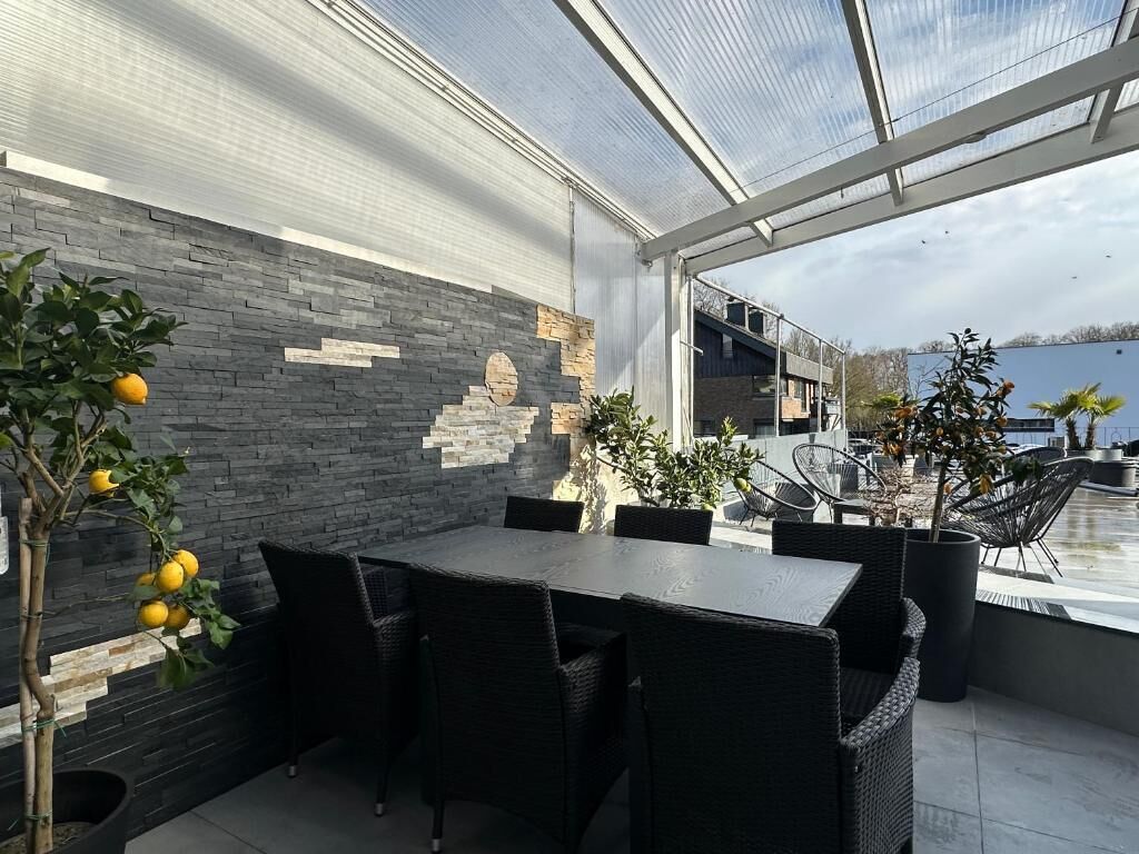 An outdoor patio with a glass ceiling, stone wall, and seating area.