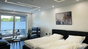 Camera da letto moderna con un ampio letto, una televisione e un balcone con sedute all'aperto.