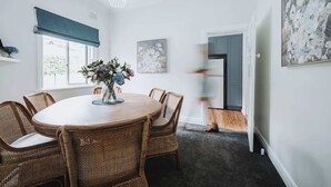 Un coin repas avec une table ronde, des chaises en osier, un vase de fleurs et un luminaire au plafond.
