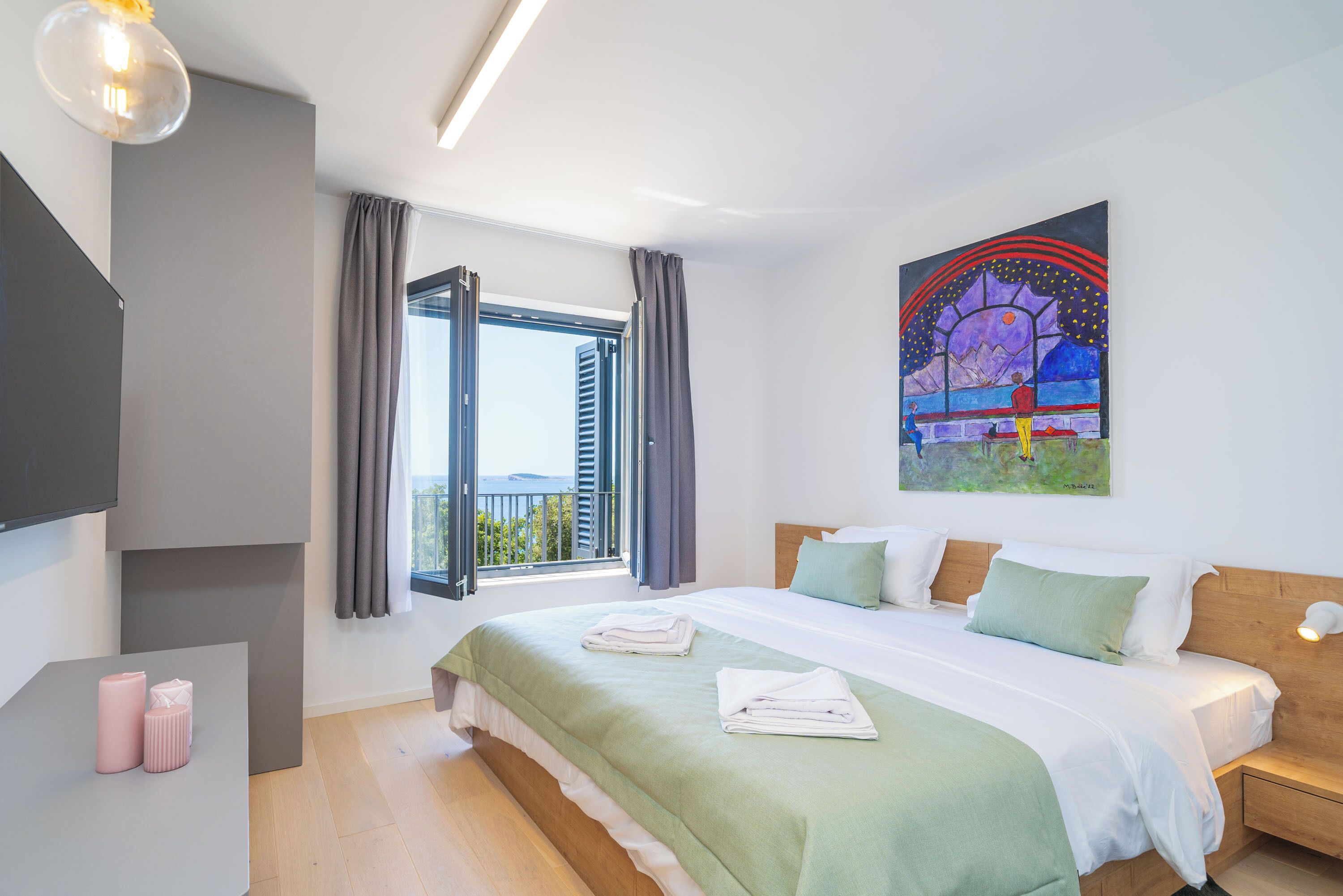 A modern hotel room with a large bed, a flat-screen TV, a window with curtains, and a painting on the wall.
