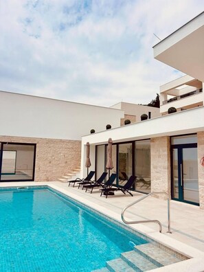 A modern pool area with a clear blue pool, lounge chairs, and a stone wall.