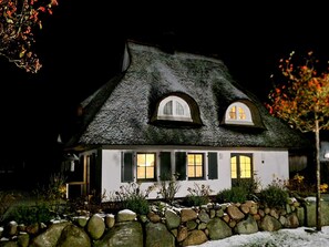 Stunning house with a thatched roof and symmetrical facade, surrounded by lush gardens and a stone wall.