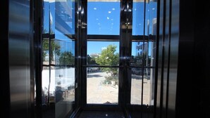 Vista a través de un ventanal que da a un espacio exterior con suelo pavimentado, algo de vegetación y un coche estacionado.