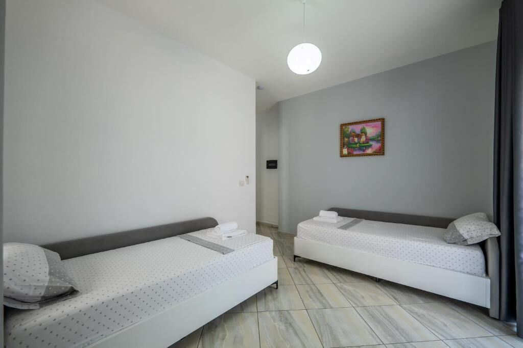 A room with two single beds, a small painting on the wall, and a light fixture.