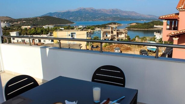 Un balcón con una mesa lista para el desayuno, con vistas a un pueblo costero y una extensión de agua.