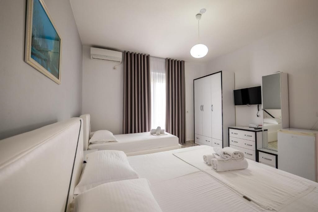 Ett hotellrum med två sängar, en TV, en garderob och ett fönster med gardiner.