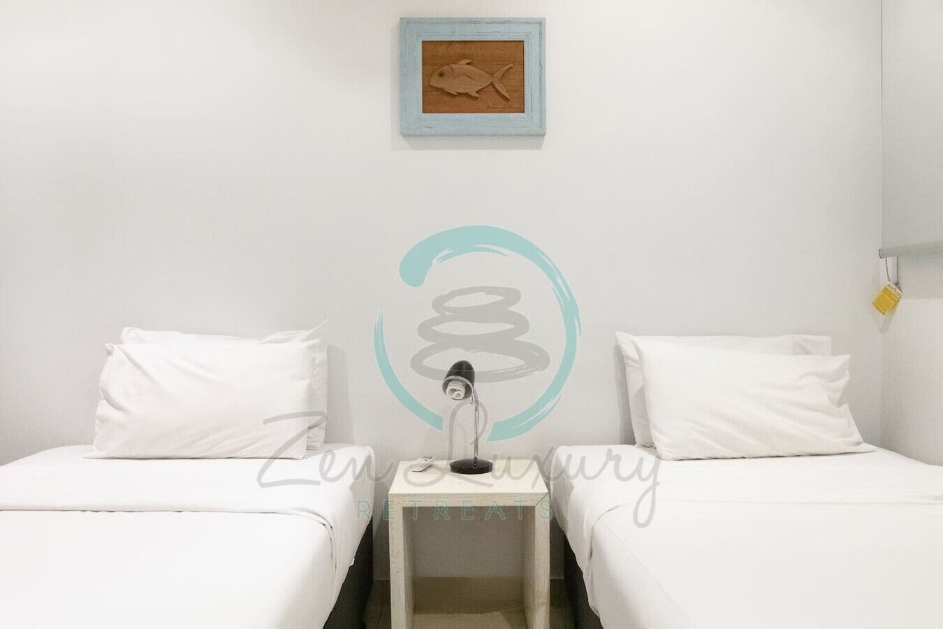 A simple room with two beds, a nightstand, a lamp, and a framed picture on the wall.