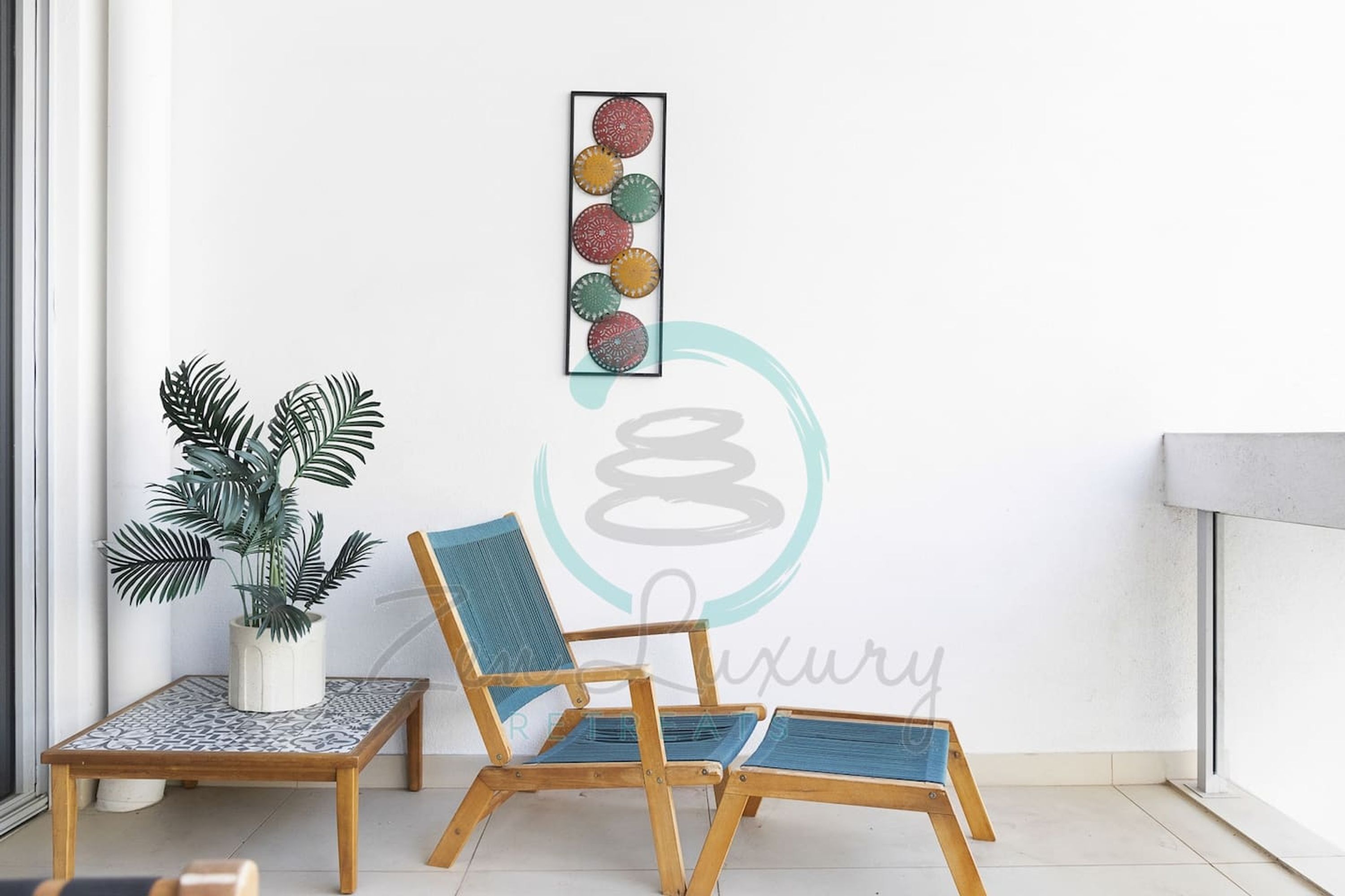 A balcony with a wooden chair and a small table, a potted plant, and a wall art piece.