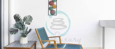 A balcony with a wooden chair and a small table, a potted plant, and a wall art piece.