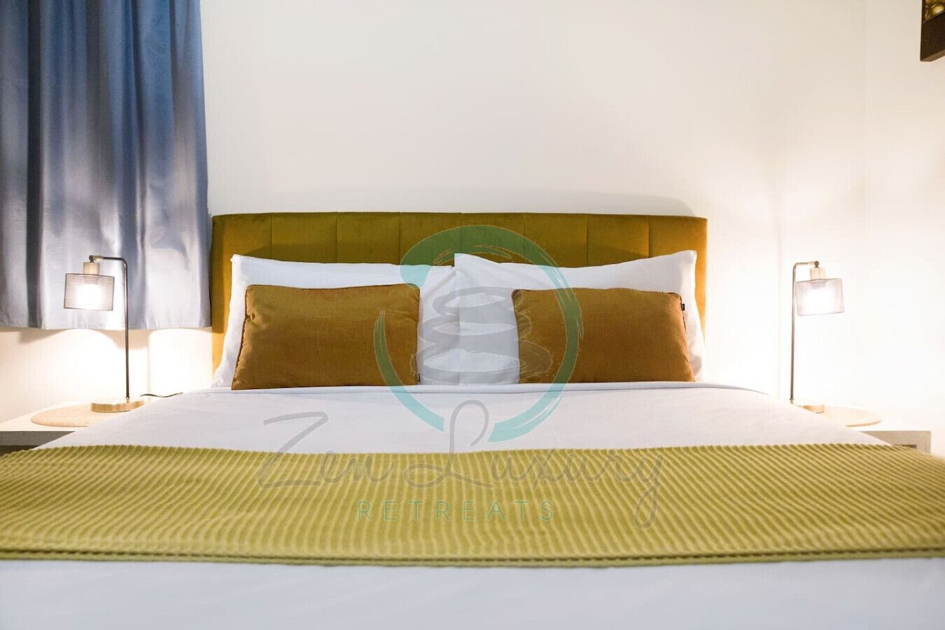 A hotel room with a bed, two bedside lamps, a headboard, and a green striped area rug.