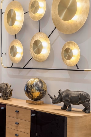Eine Wandleuchte mit geometrischem Design sowie eine Globus- und Nashornskulptur auf einem Holzboden.
