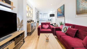 A modern living room with a large flat-screen TV, red sofas, a wooden coffee table, and a kitchen in the background. - Alexandra's Unique Apartment (Athens)
