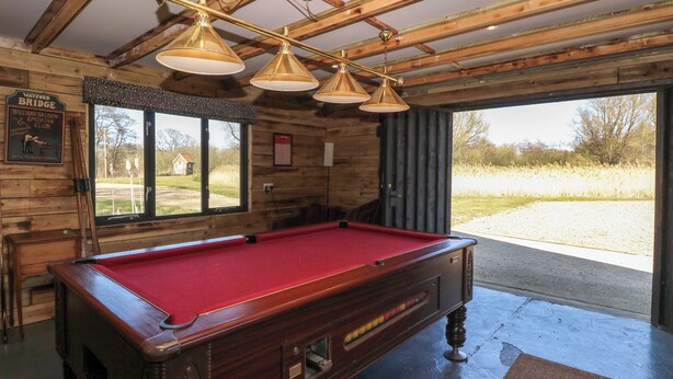 A pool table in a room with wooden beams and a large window. - Wayford Mill (Norwich)