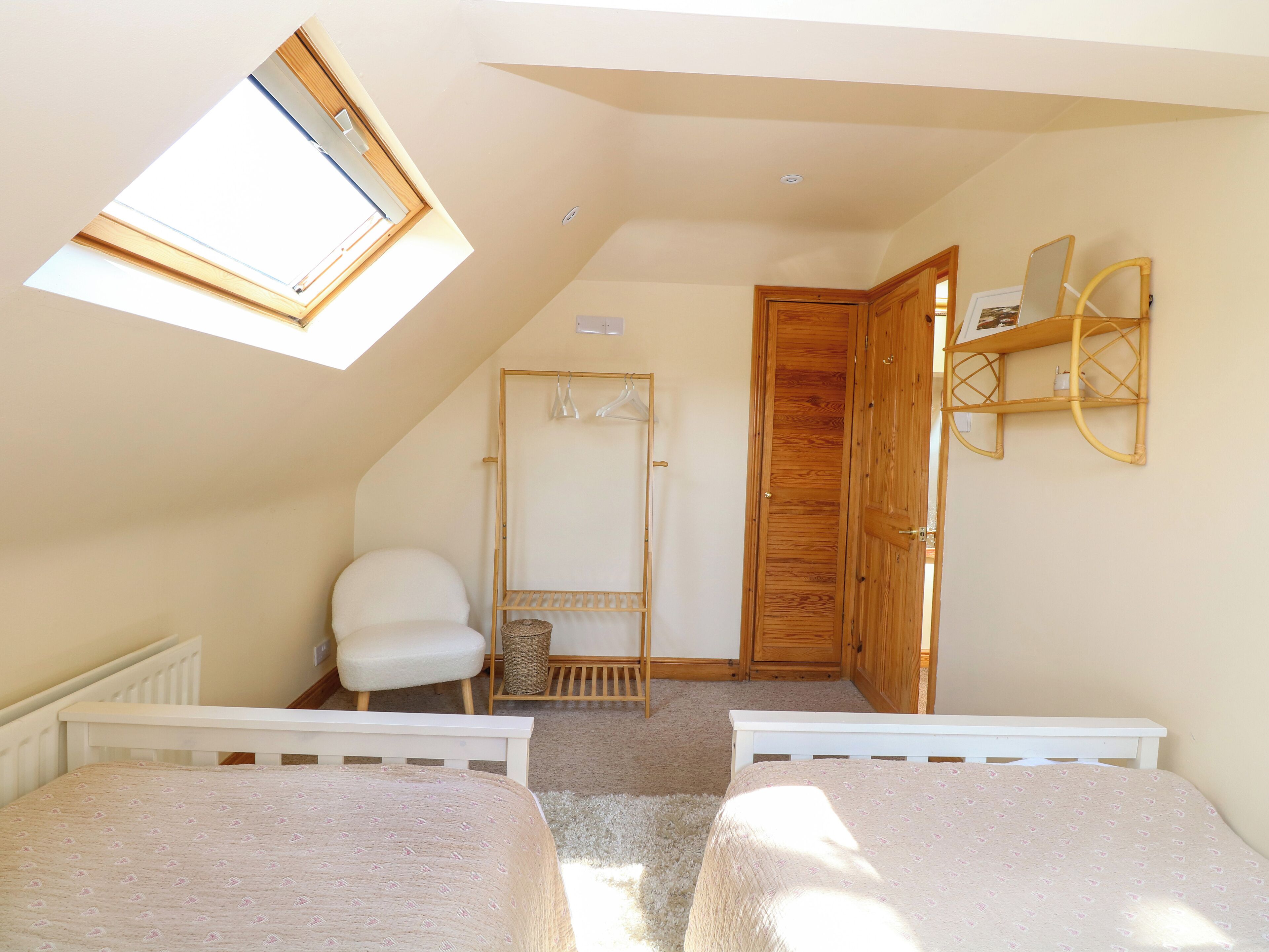 Une chambre avec deux lits, une lucarne, une armoire en bois et une chaise blanche.
