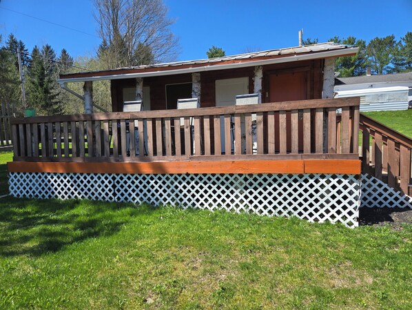 A wooden deck with a white lattice base, a porch, and a small attached structure. - Charming cabin in delightful Watkins Glen with AC and beautiful surroundings. (Watkins Glen)