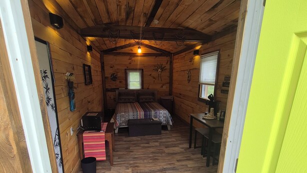 A cozy wooden cabin bedroom with a bed, a desk, and a bright yellow door.
