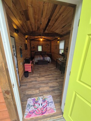 A cozy wooden cabin bedroom with a bed, a desk, and a bright yellow door. - Charming cabin in delightful Watkins Glen with AC and beautiful surroundings. (Watkins Glen)